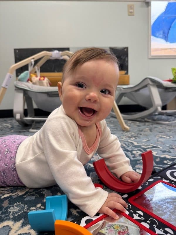 Smiling Amici infant on the classroom rug during floor time